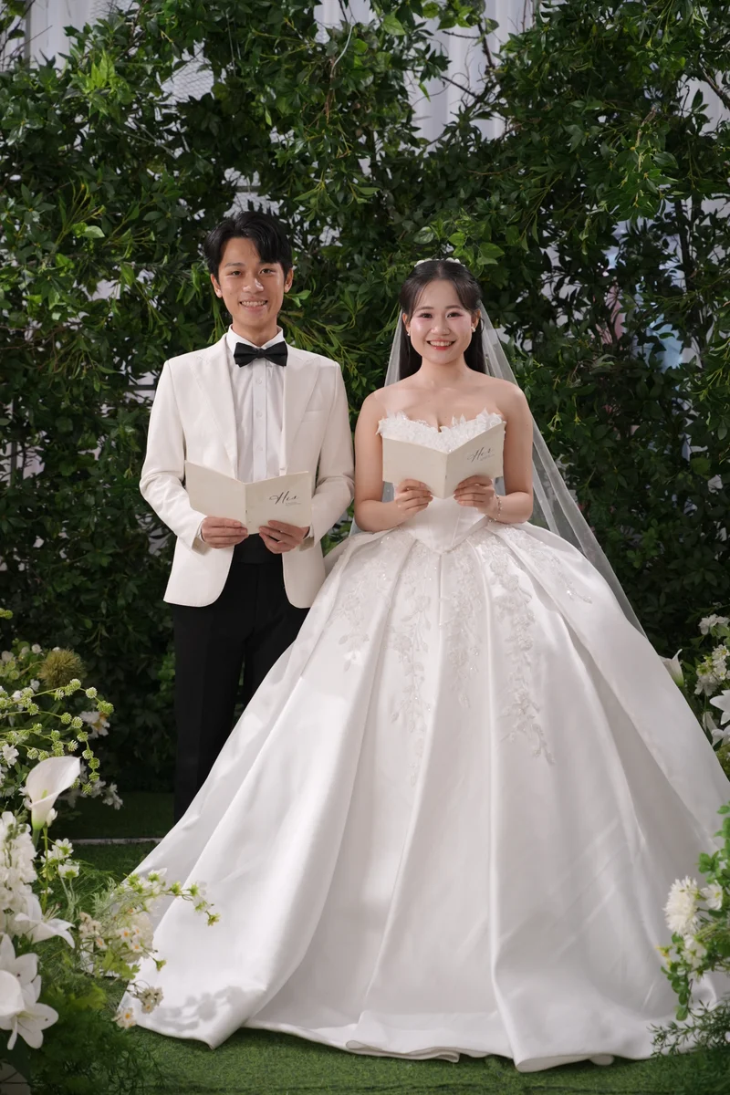 Duy và Ánh đứng cạnh nhau, cùng cầm thiệp giữa khu vườn