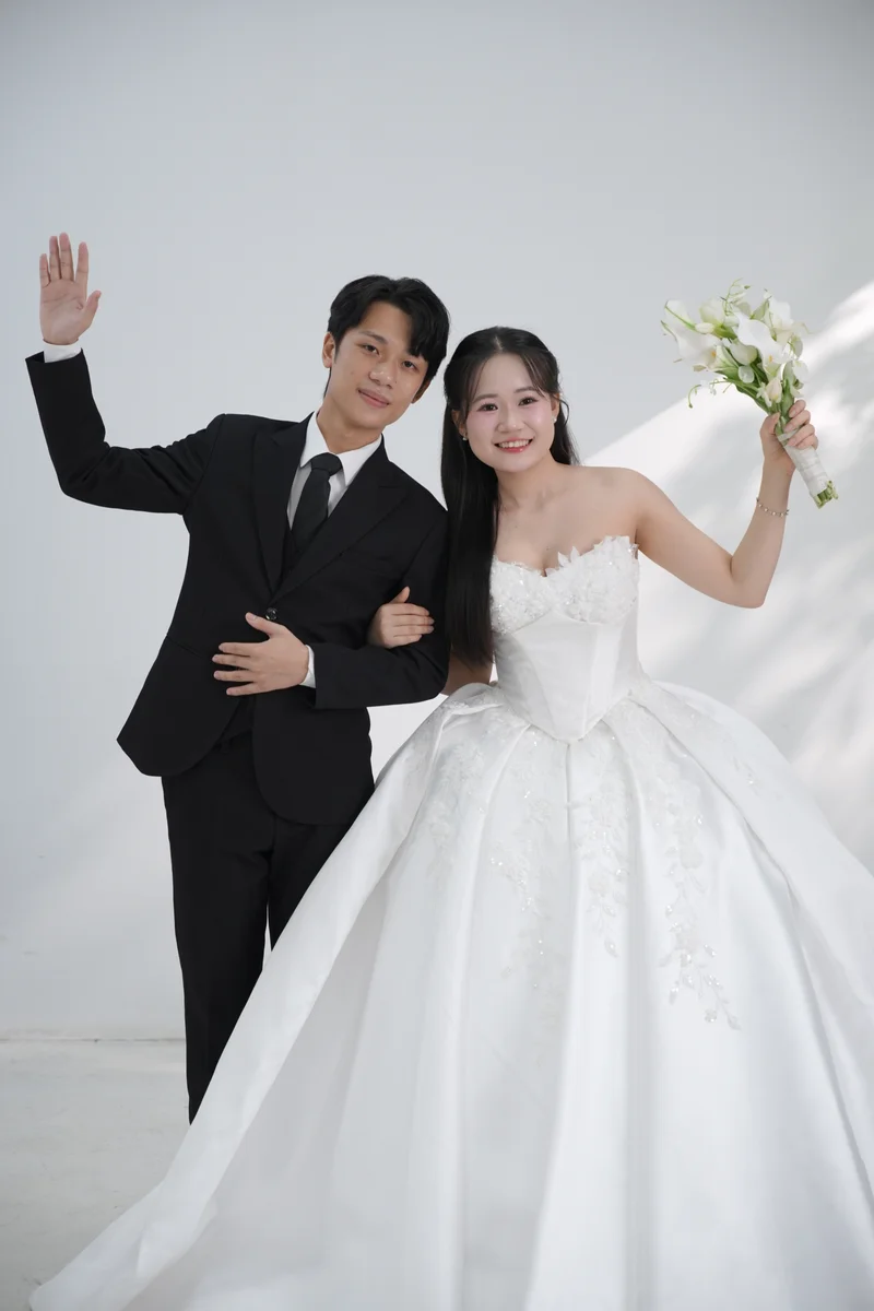 Duy và Ánh nghiêng đầu bên nhau, giơ tay và bó hoa trong bộ ảnh trắng