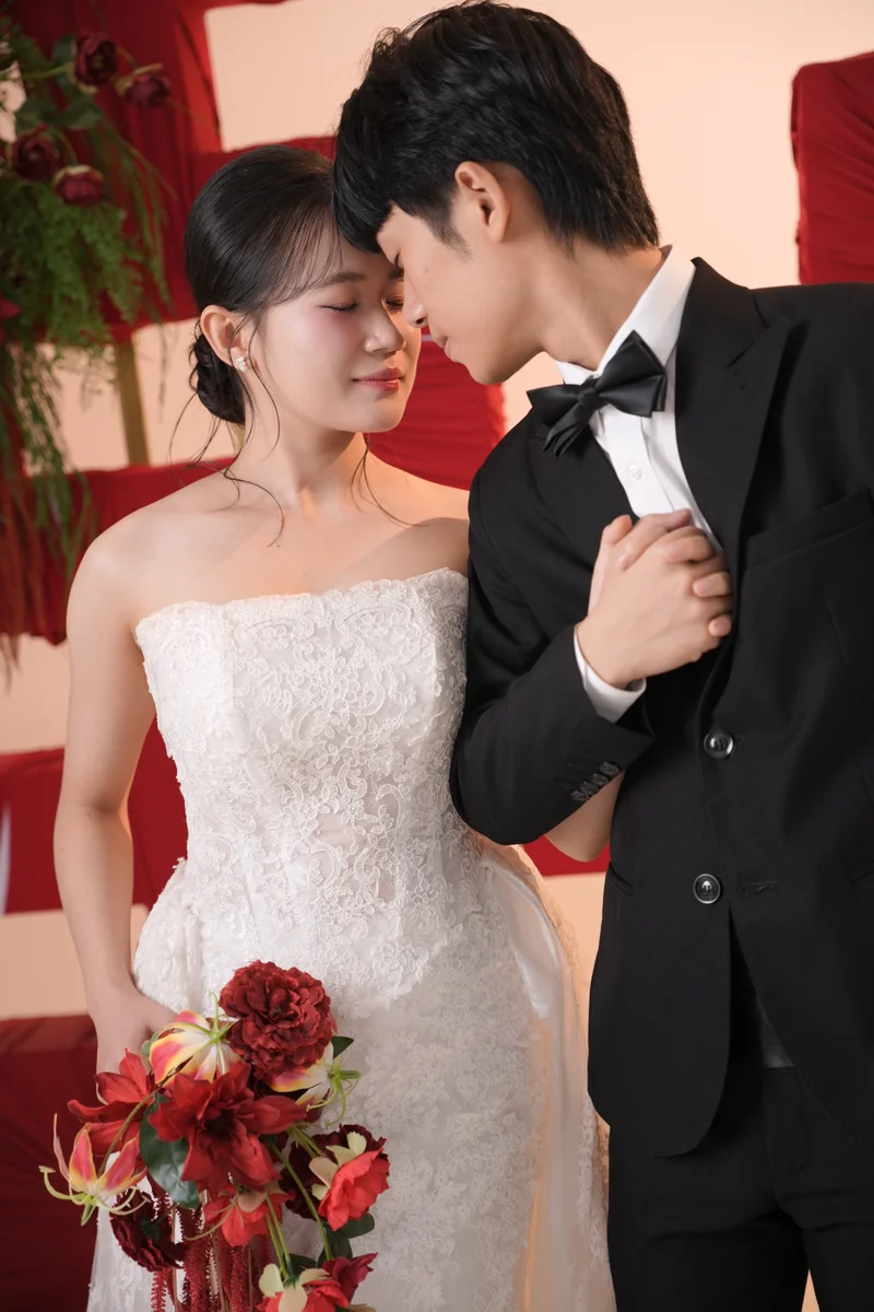 Duy tựa trán bên Ánh trước phông chữ hỷ đỏ, cô dâu cầm hoa đỏ